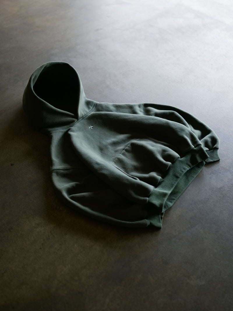 Model wearing Goji Longevity forest green organic cotton unisex hoodie — streetwear styling